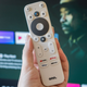 A hand holding up the Onn FHD Streaming Stick's white remote with too many buttons